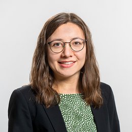 Headshot of Anna Lena Köttig, a young woman smiling on a simple light gray background.