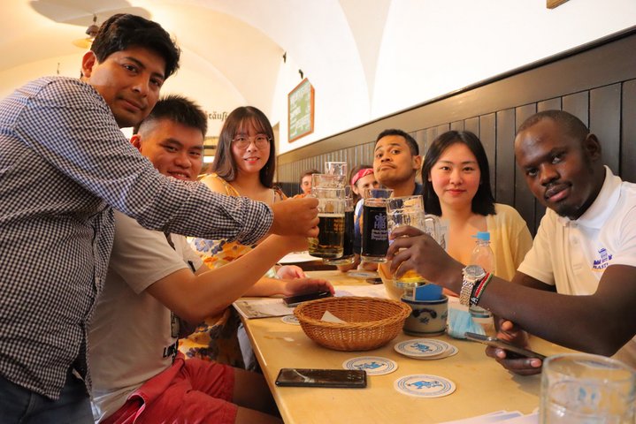 Diverse students of the international summer school 2022 sitting in a bavarian wirtshaus drinking beer.