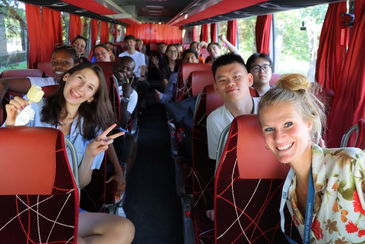 Diverse students of the international summer school 2022 sitting in a bus and smiling at the camera.
