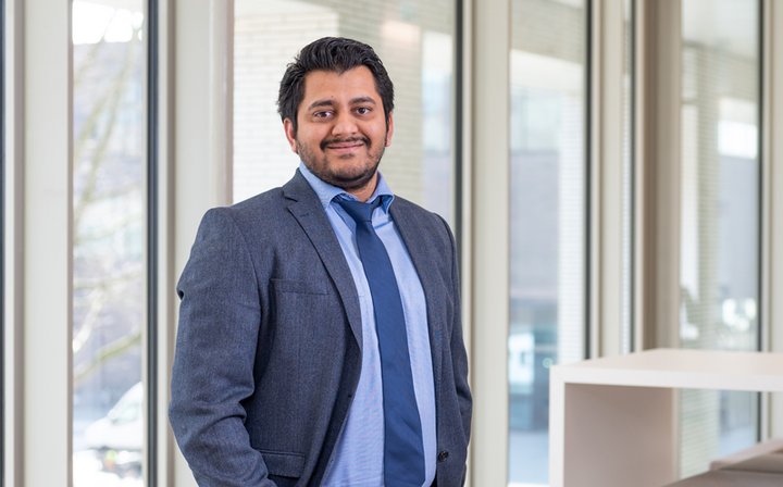 Phd candidate Sairam Siraman is standing in a bright building wearing a blue suit, a light blue shirt and a blue tie.