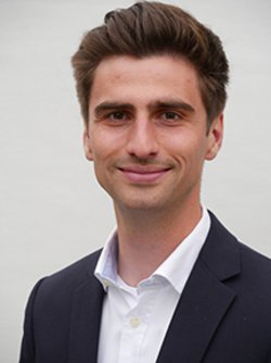 Jonah Sellner, a young man in a black suit and a white shirt smiles at the camera