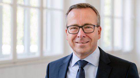Headshot of Prof. Gunther Friedl, standing inside the university in a blue suit smiling at the camera.