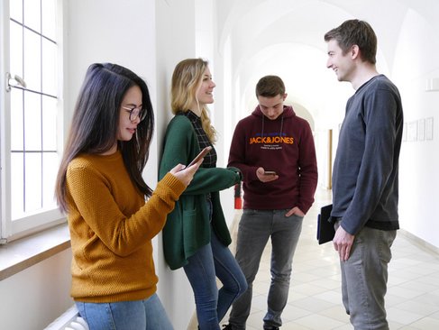 four students which include two girls and two boys talking to each other while standing in the corridor 