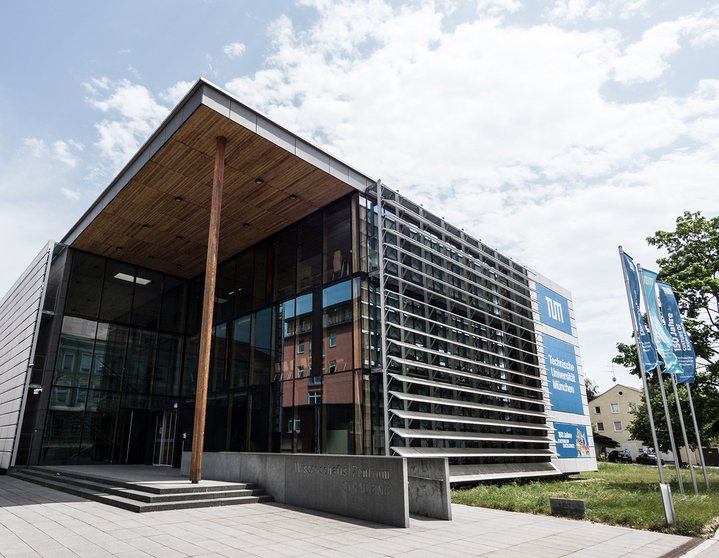 A glass building with wooden roof and surrounded by tress 