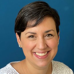 Headshot of Christine Vogt-Bolch, a woman smiling on a simple dark blue background.