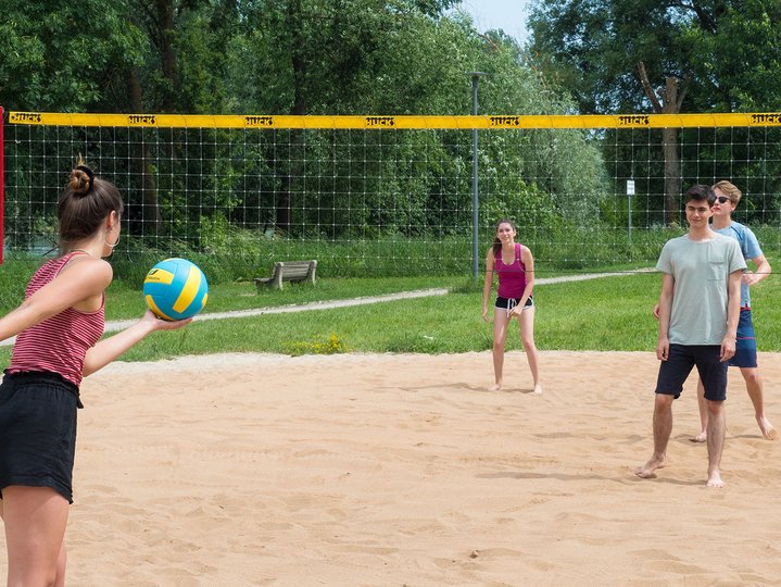 four student playing volleyball on the sand