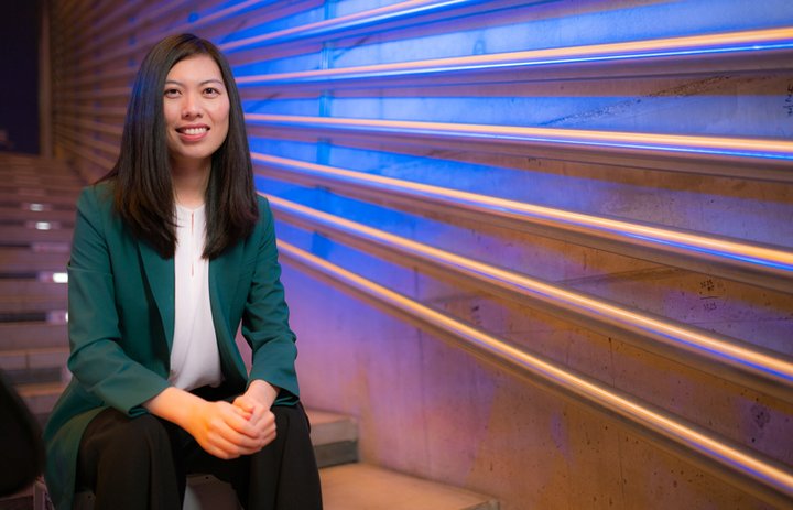 Prof. Dr. Amy Zhao-Ding is sitting in an illuminated stairway wearing a green blazer, a white shirt and black pants.