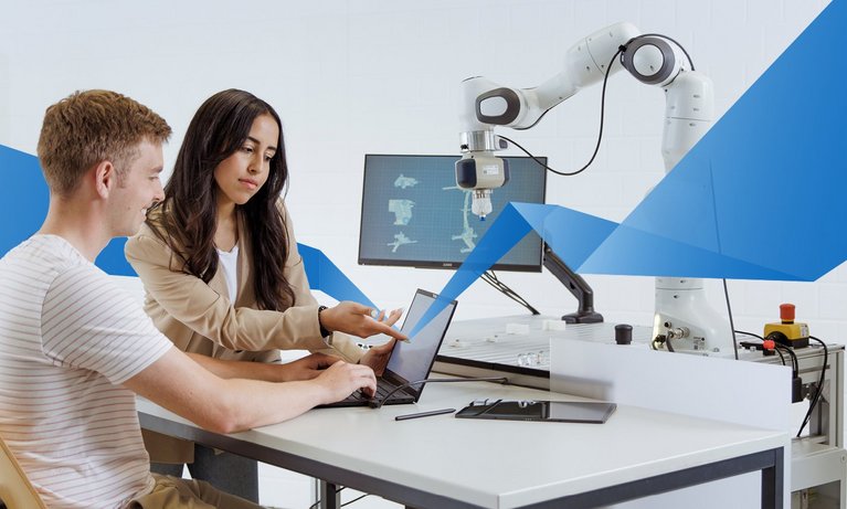 A hispanic female student and a caucasian male student are sitting at a table in a digital lab and looking at a laptop.