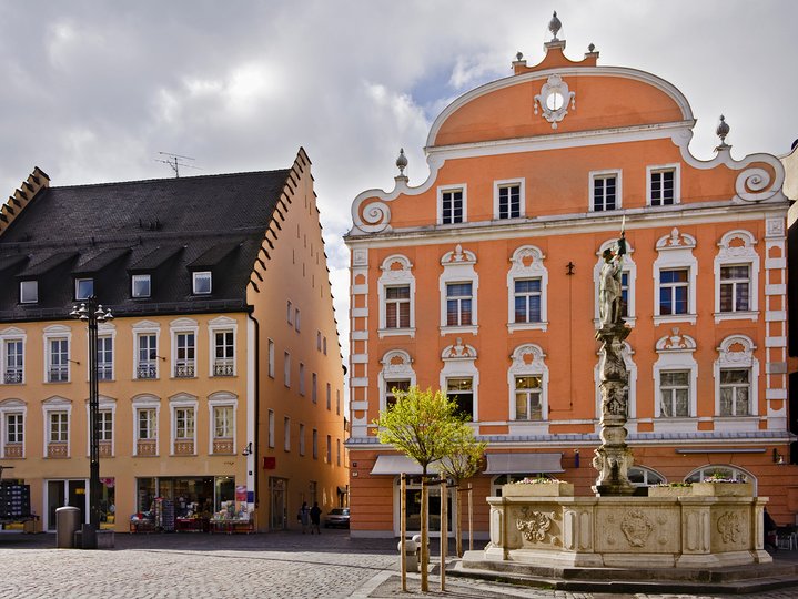 A tall statue in the middle of the street with two buildings on its left side