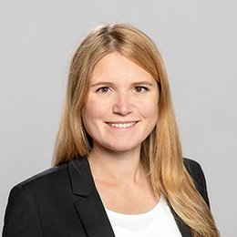 Headshot of Charlotte Bayer, a young woman smiling on a simple grey background.