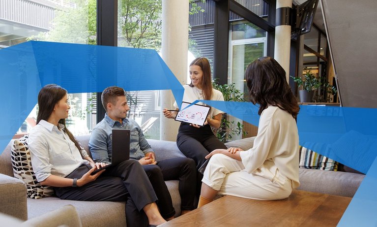 Three female and one male student are sitting in a lounge. One student holds a tablet and shows something on it.