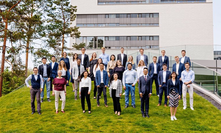 The team of the Center for Digital Transformation stands on a hill at the TUM campus Heilbronn in front of a building.