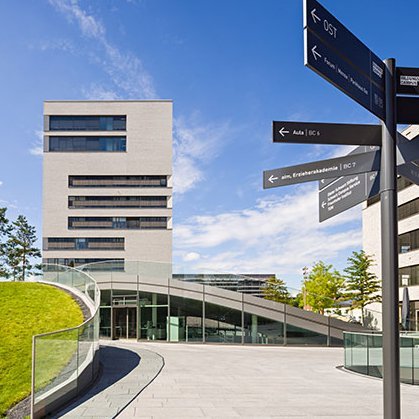 View of TUM Campus Heilbronn, looking at a tall building, the so-called L-building. In front is a signpost.