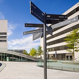View of TUM Campus Heilbronn, looking at a tall building, the so-called L-building. In front is a signpost.