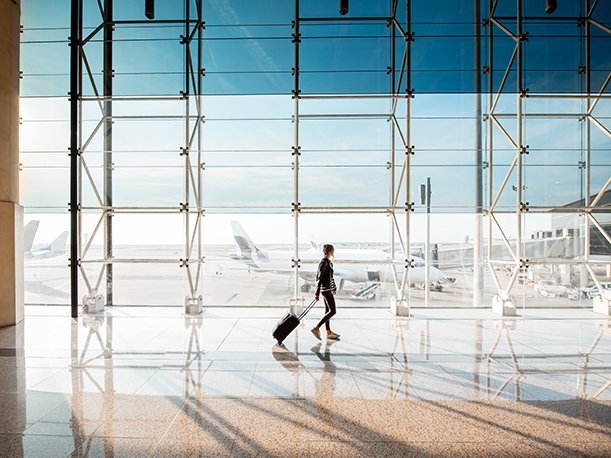 View on the aiport window with woman walking with suitcase at the departure hall of the airport. Wide angle view.