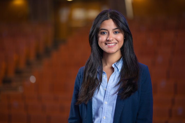 Phd candidate Sofia Abid is standing in a movie theatre wearing a blue blazer and a light blue blouse.