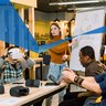 Young woman who is the leader of the project speaking to her colleagues standing near the white board. Diverse team wearing virtual reality glasses in office sitting at the table in an entrepreneurial and innovative enviroment.