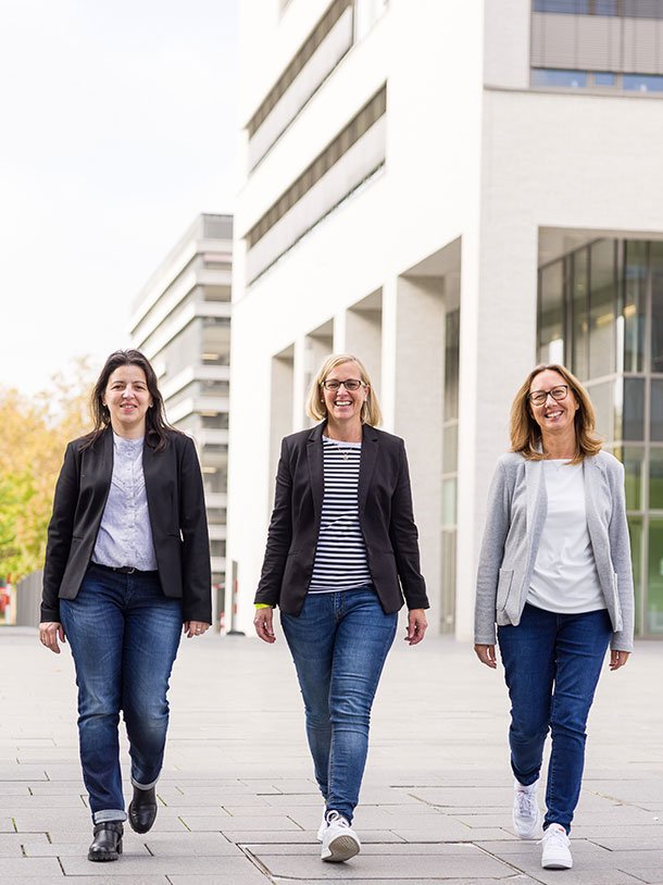 The TUM Campus Heilbronn student service point team: Vanesa González Taboada, Beate Polap and Nicole Jäger, walking towards the camera. Behind them: the so-called L-building at TUM Campus Heilbronn.