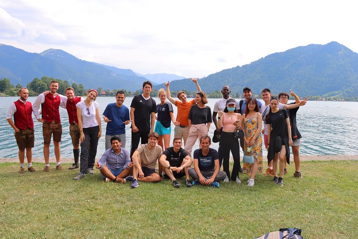 Group picture of diverse students of the international summer school 2022 on a lake with mountains in the background.