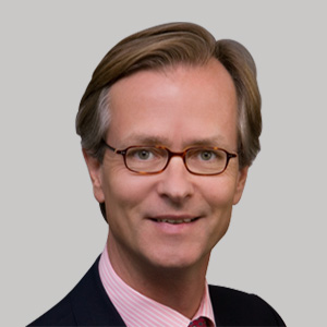 Headshot of Robert von Weizsäecker, a midle-aged man in a suit on a simple light gray background. 