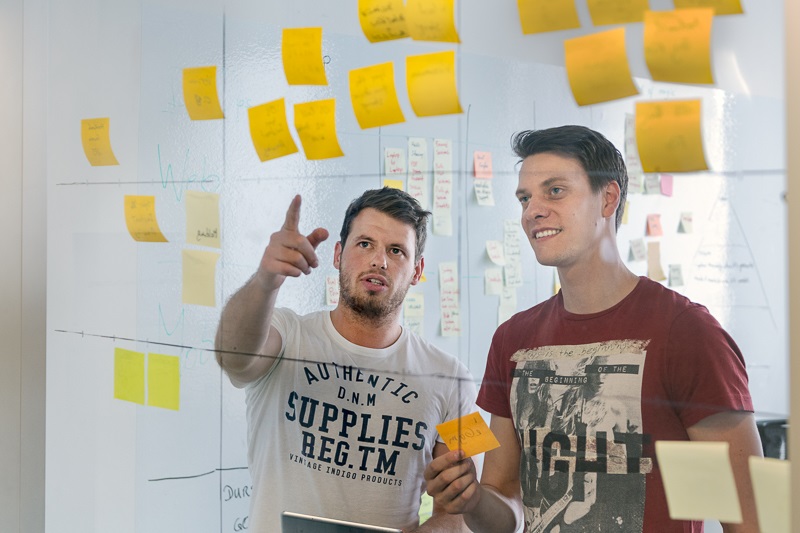 Two men in front of transparent screen with post-it notes