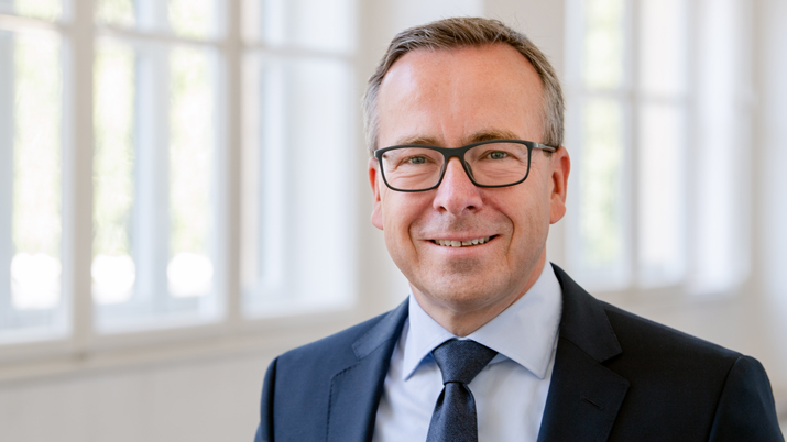 Headshot of Prof. Gunther Friedl, standing inside the university in a blue suit smiling at the camera.