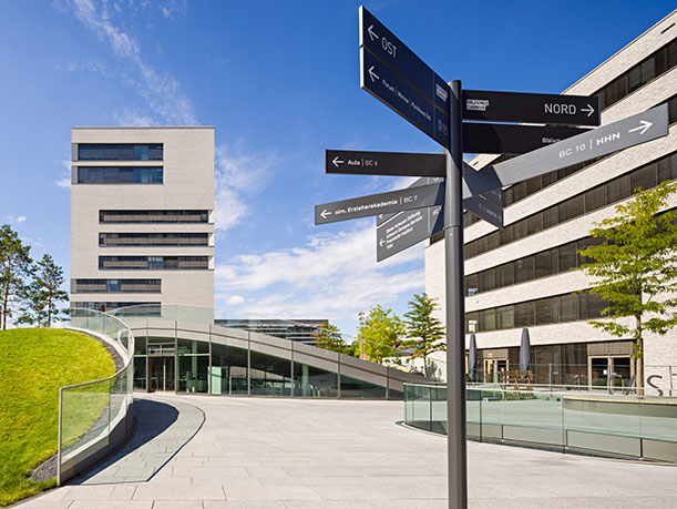 View of TUM Campus Heilbronn, looking at a tall building, the so-called L-building. In front is a signpost.