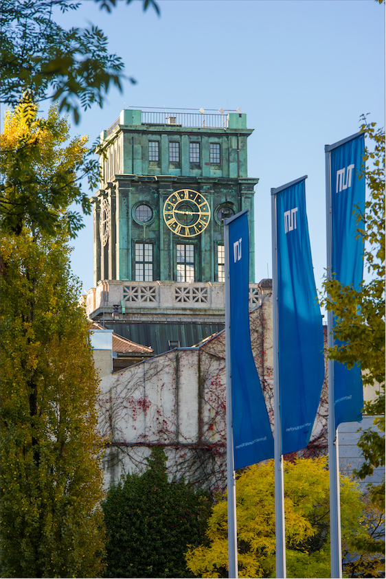 The Thiersch Turm, a clock tower with TUM flags in front of it at the campus in Munich.