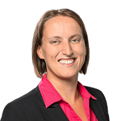 Portrait of our grade manager Janine Rothenburger. She has blonde hair, wears a pink blouse and a black blazer and smiles at the camera.