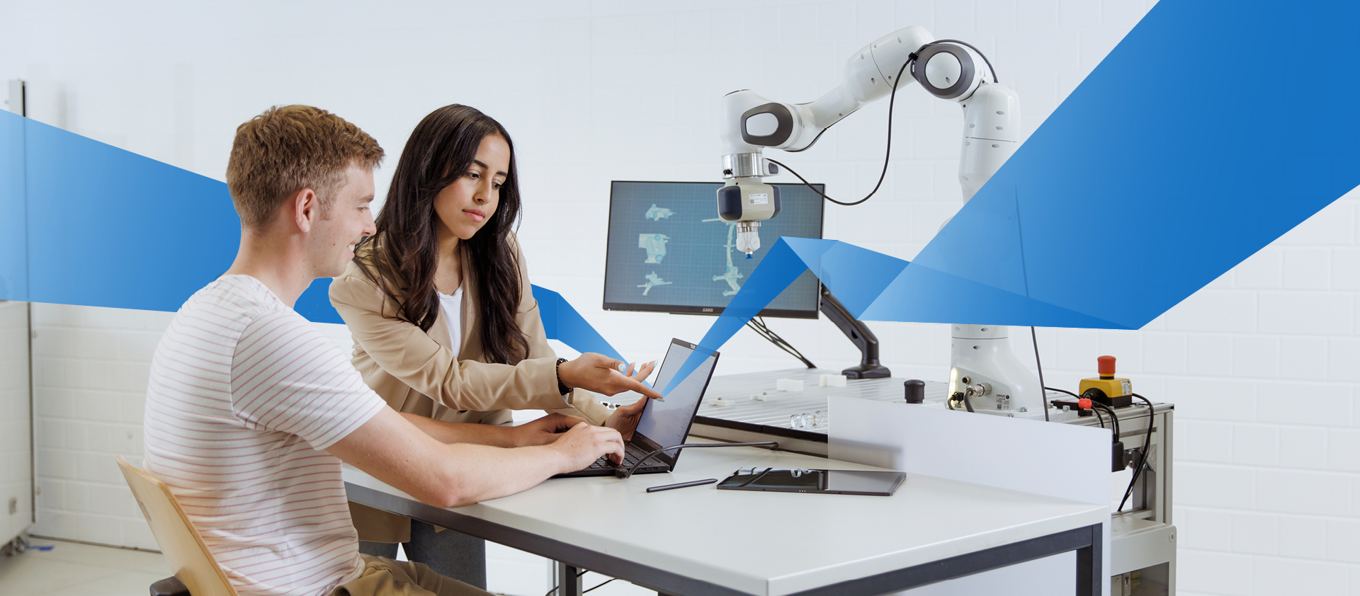 A hispanic female student and a caucasian male student are sitting at a table in a digital lab and looking at a laptop.