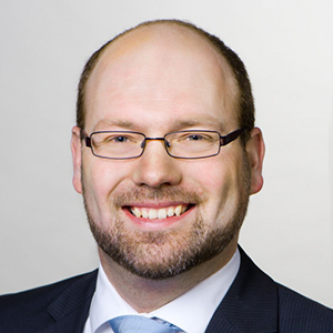 Headshot of Prof. Dr. Philipp Maume, S.J.D., a middle age man smiling on a simple background.